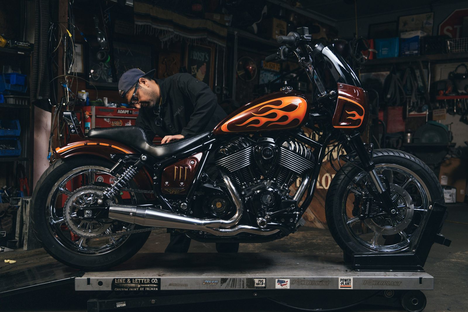 A motorcycle builder working on a custom orange Indian motorcycle with flame paintwork on a workshop lift