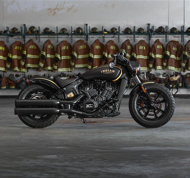 Jack Daniel's Limited Edition Indian Scout Bobber in black with gold accents, displayed in a garage with firefighter turnout gear hanging on the wall